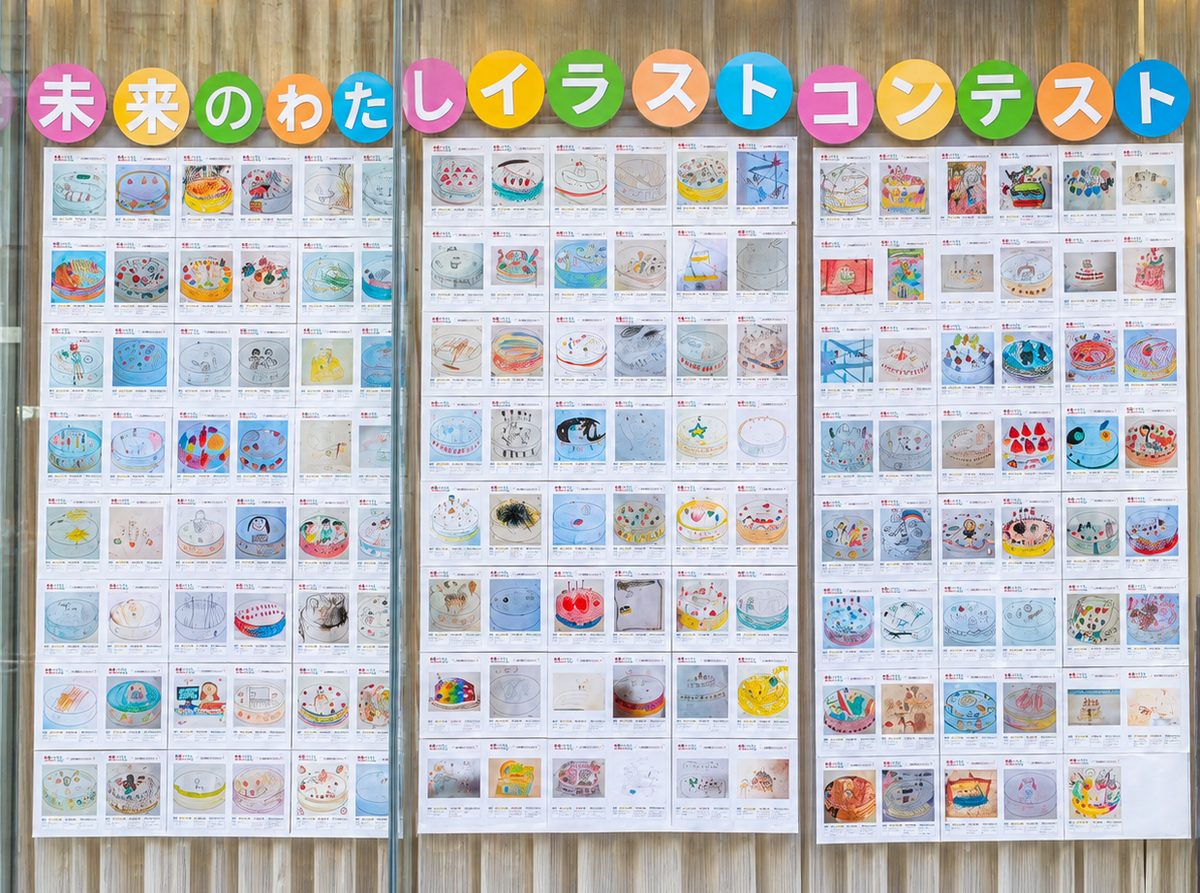 旭会の公式サイトで公開された、ガラス窓に並ぶ「未来のわたしイラストコンテスト」の応募作品。上部に色とりどりの丸い文字でコンテスト名が掲げられ、その下にケーキを描いたイラストが3つの面に並ぶ