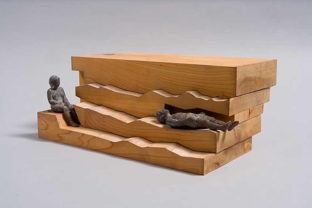 DIGINNER GALLERY の展覧会ページで公開された北山翔一の作品。波形に彫った板を重ねた木彫に、黒い小さな人の像が腰掛け、横たわる
