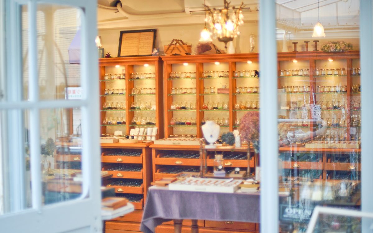 ガラス戸越しに見える店内。木の棚にパーツの入った小瓶が並び、シャンデリアが下がる
