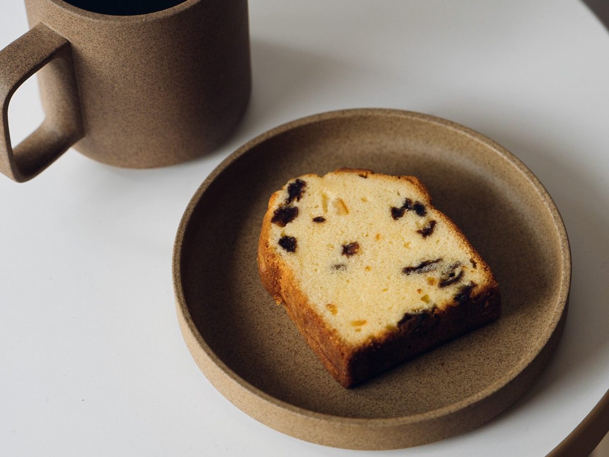 ドライフルーツやナッツを混ぜ込んだパウンドケーキ状の焼き菓子のスライスとコーヒーカップ