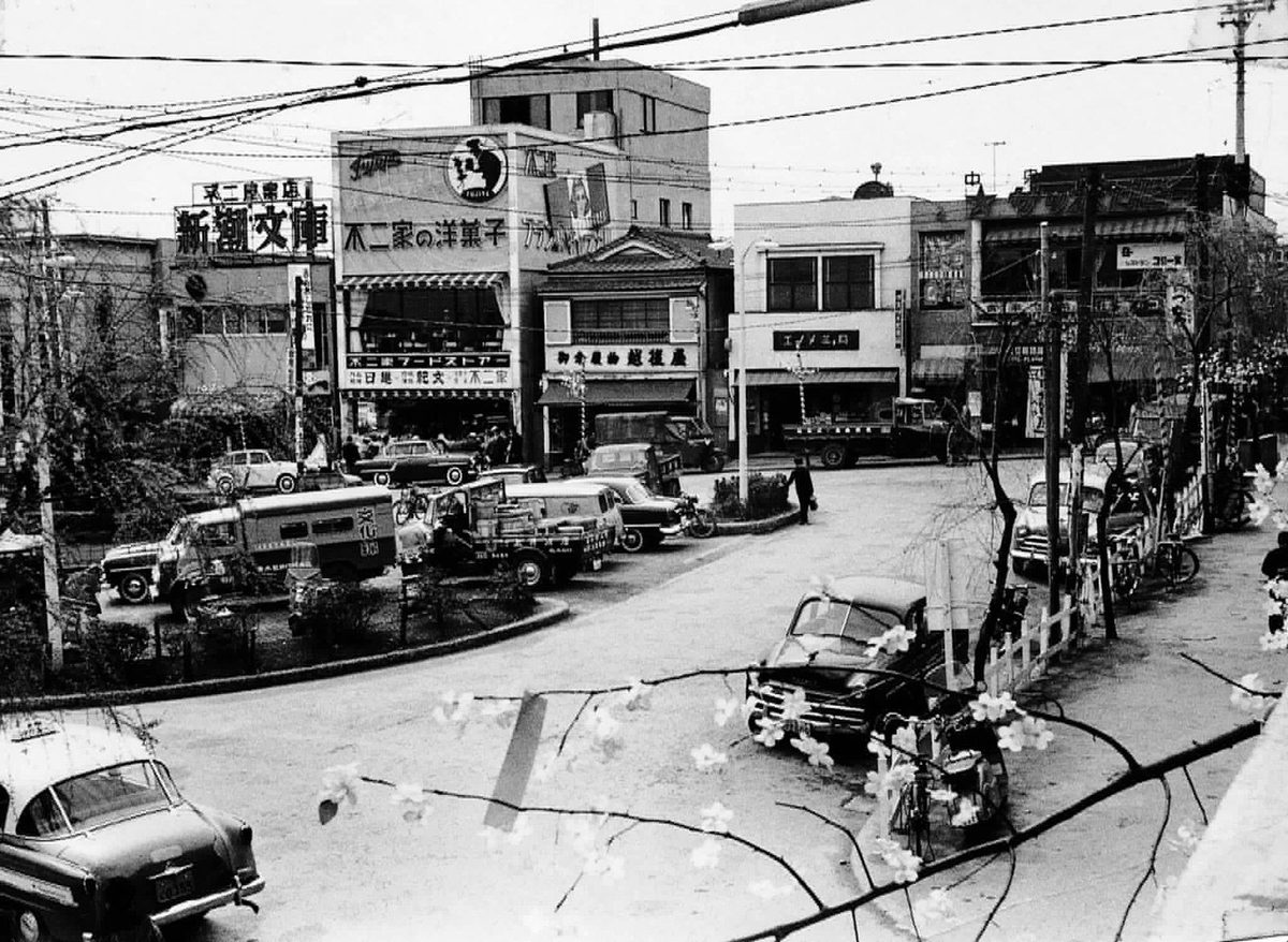 東急公式サイトの沿線記事で公開された、1950年代の自由が丘駅前の白黒写真。ロータリーに車が並び、左上の建物の看板に「不二屋書店」「新潮文庫」、その右の建物に「不二家の洋菓子」の文字が見える