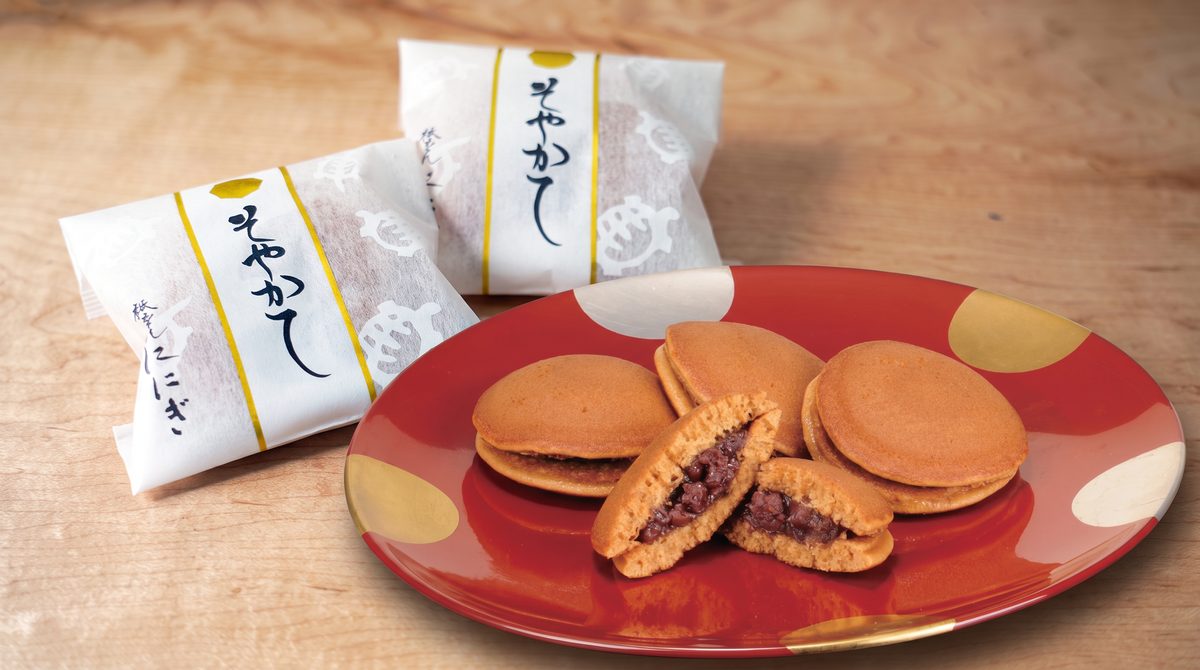 プレスリリースで公開されたキャンペーン贈呈品「黒糖どら焼き そやかて」の商品ビジュアル。赤い和皿に3個並び、断面からは小豆あんが見える