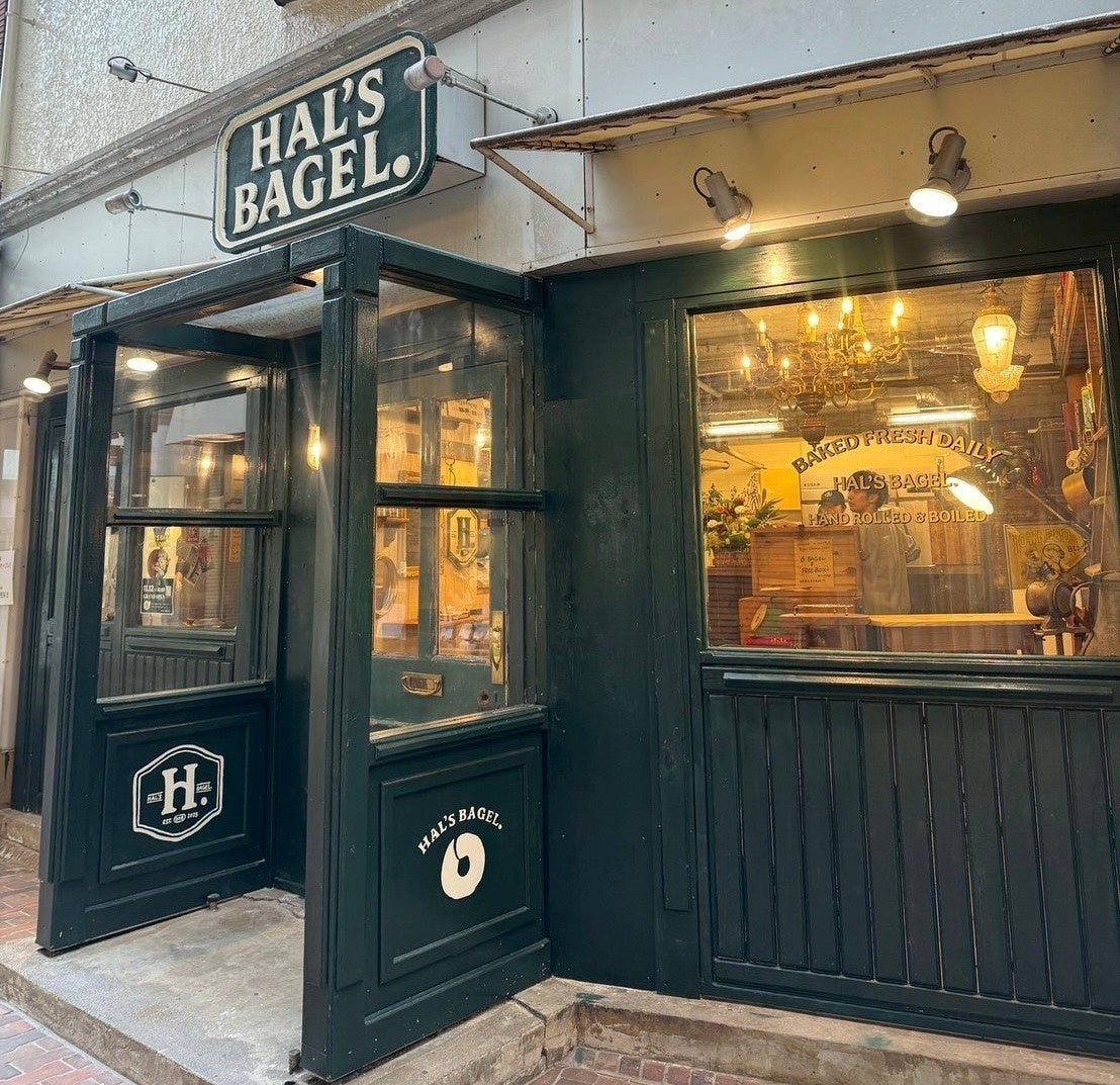 濃い緑色の木枠でしつらえた店舗の外観。上部に「HAL'S BAGEL.」の看板、窓ガラスに「BAKED FRESH DAILY」「HAND ROLLED & BOILED」の文字、店内にシャンデリアが下がる