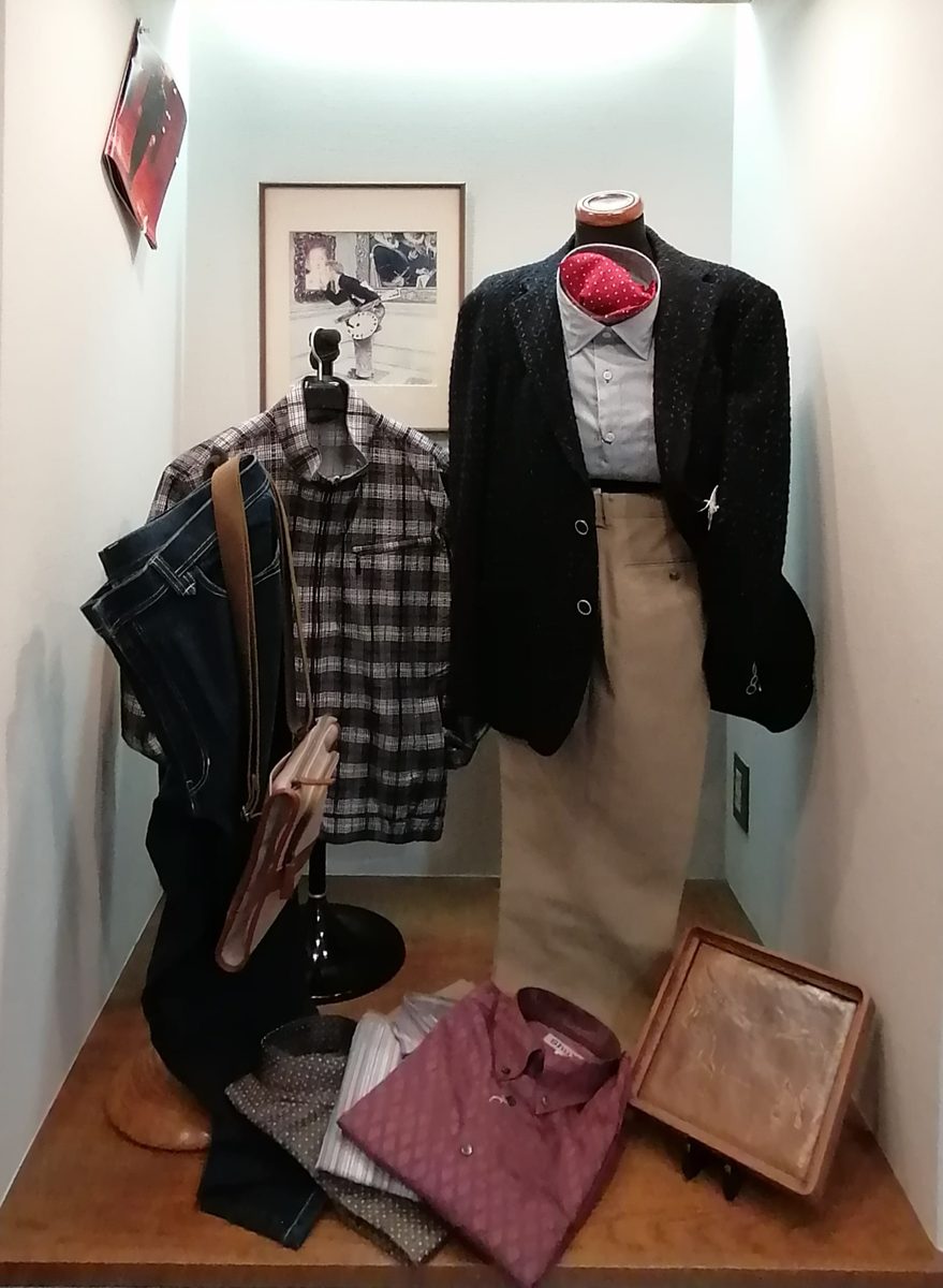 店舗ページに掲載された写真。白い壁の一角に、ジャケットとシャツを着せたトルソー、チェックのシャツとジーンズ、革のバッグが飾られ、手前にたたんだシャツが置かれている