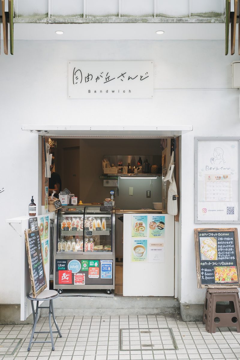白い壁に「自由が丘さんど Sandwich」の看板。間口いっぱいに開いた窓口の中にサンドイッチのショーケースが置かれ、脇に黒板のメニューが立てかけてある