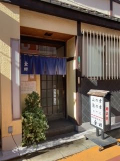 商店街公式ガイドに掲載された金田の店頭の写真。格子戸の入口に「金田」と白く染め抜かれた紺の暖簾が掛かり、脇に植え込みと、「金田」の文字が入った置き看板がある。