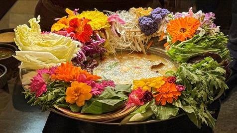 岡田不動産のプレスリリースで、Hoa Hoa のディナー「花鍋」として公開された写真。鍋の縁を色とりどりの食用花と野菜が囲んでいる