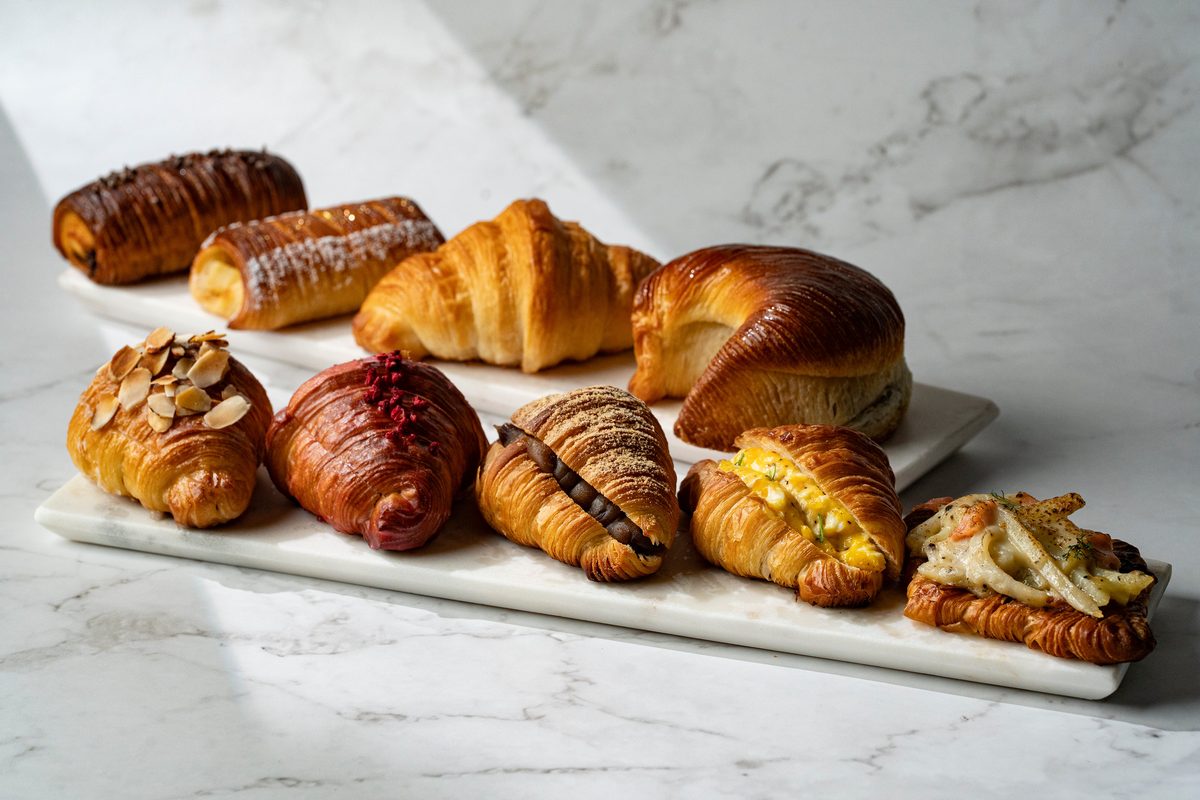 大理石の台の上に並ぶミセスパブロフベーカリーのパン。チョコレート、アーモンドスライス、抹茶、ラズベリー、卵サラダ、スモークサーモンなどをはさんだ小ぶりのクロワッサンとメロンパン、パンオショコラが計9種