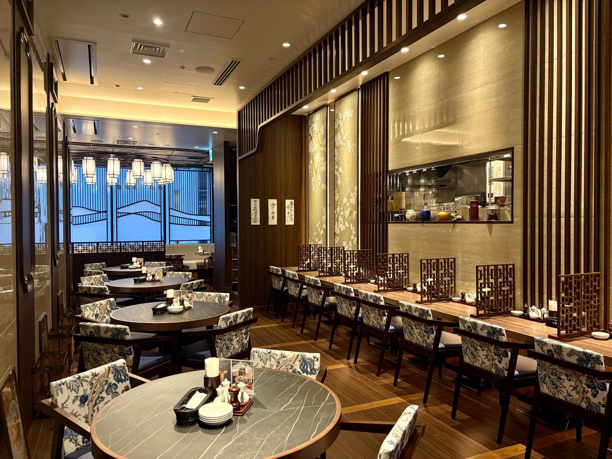 プレスリリースで公開された香華園の店内。円卓と壁沿いのカウンター席、青と白の花柄チェア