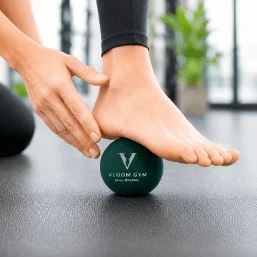 VLOOM GYM のロゴが入った緑色のボールに片足を乗せ、手で足首を支える様子