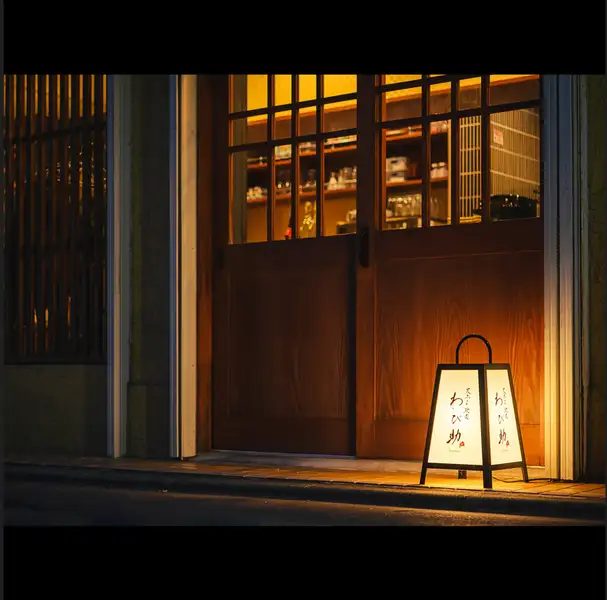 天ぷら馳走 わび助の公式サイトで公開された写真。格子のガラス窓がはまった木の扉の前に、「わび助」と書かれた行灯型の看板が灯っている。上下に黒い帯がある